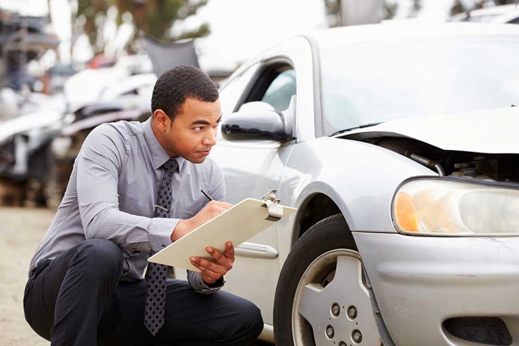 Driver reviews auto insurance documents beside a damaged vehicle after a roadway collision.